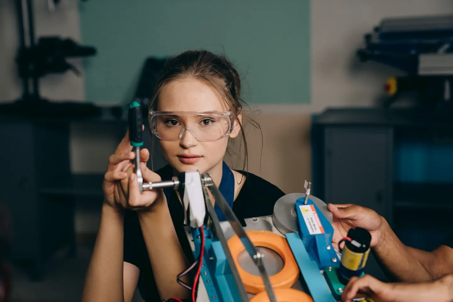 A woman wearing safety goggles adjusts equipment with a socket wrench.