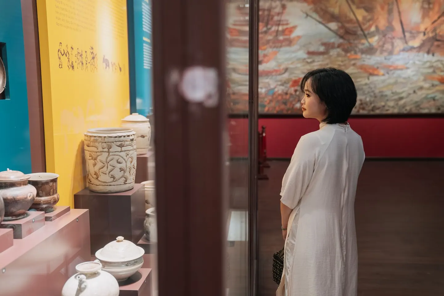 A visitor looks at ceramic vessels displayed behind glass in a museum gallery.