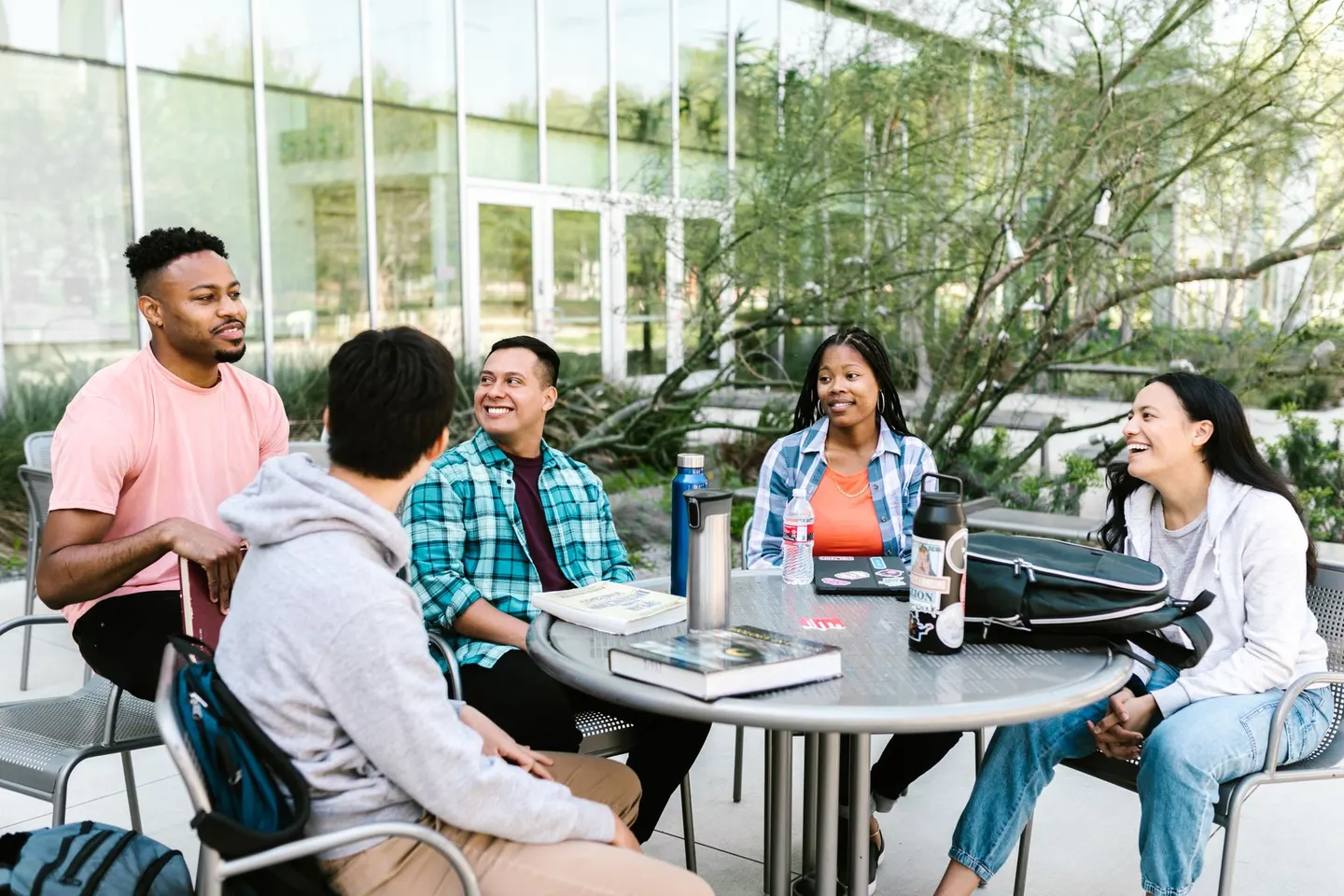 A group talking around an outdoor table with notebooks and backpacks.