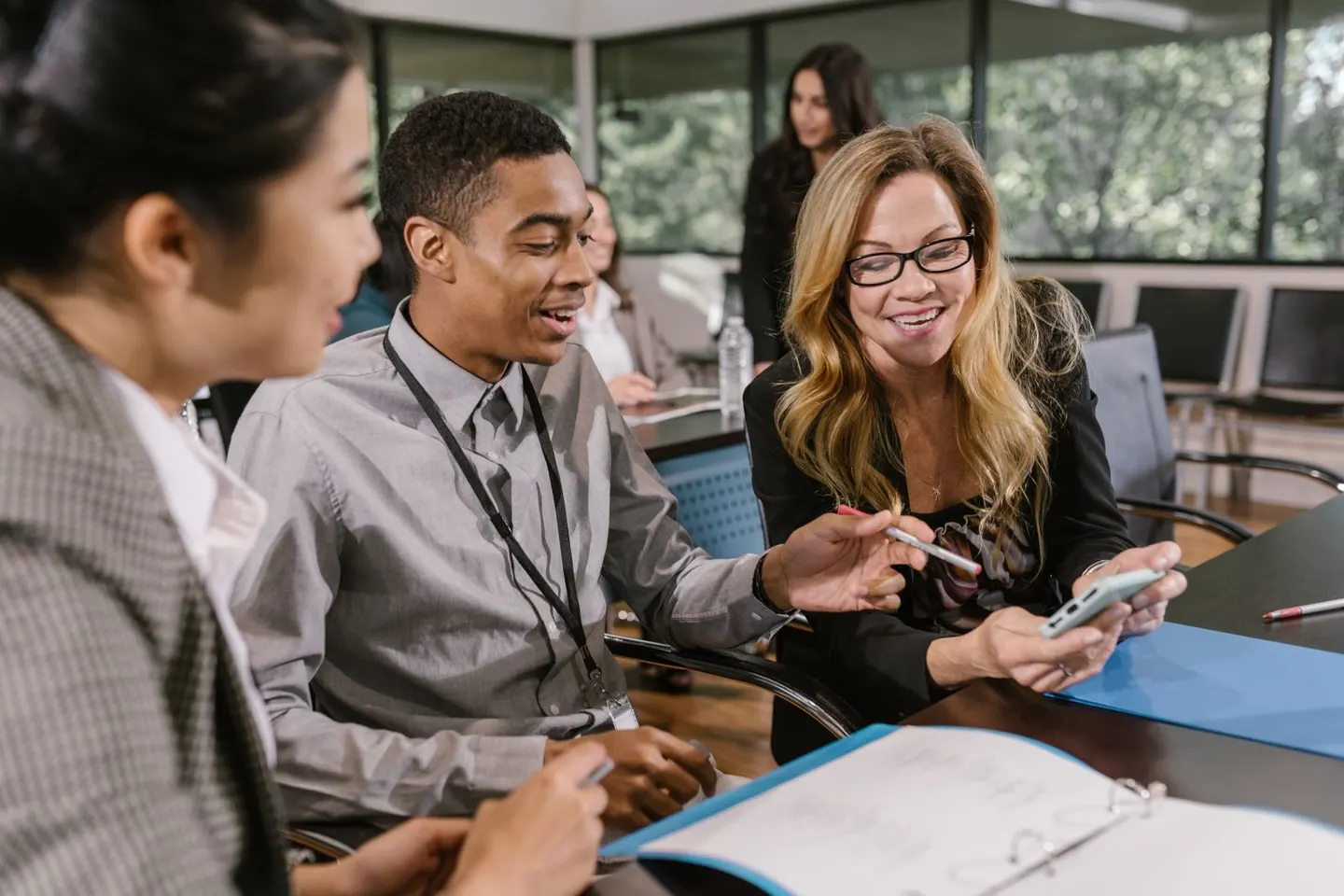 Three people discuss a tablet around a table with notebooks in a bright office.