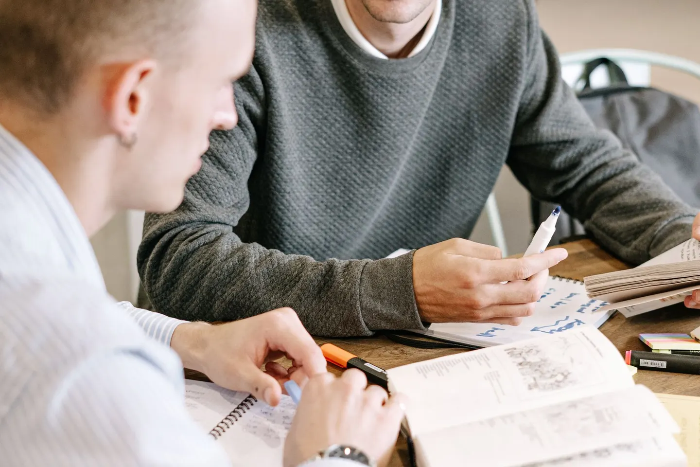 Two men discussing open books and handwritten notes at a table.