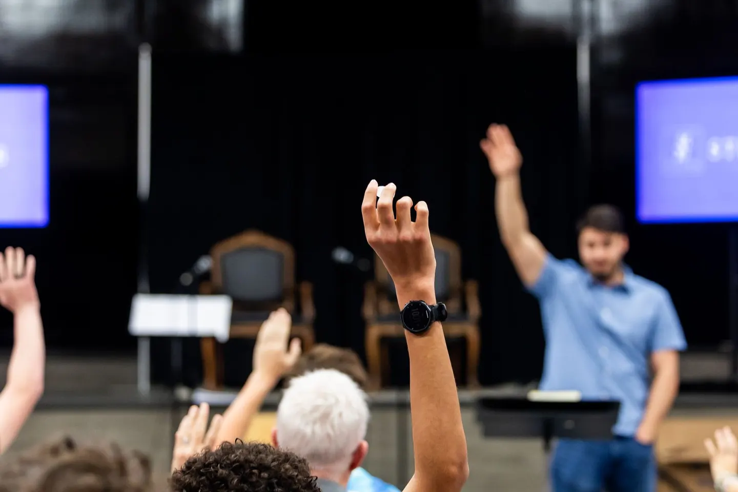 People raising their hands during an indoor classroom presentation.