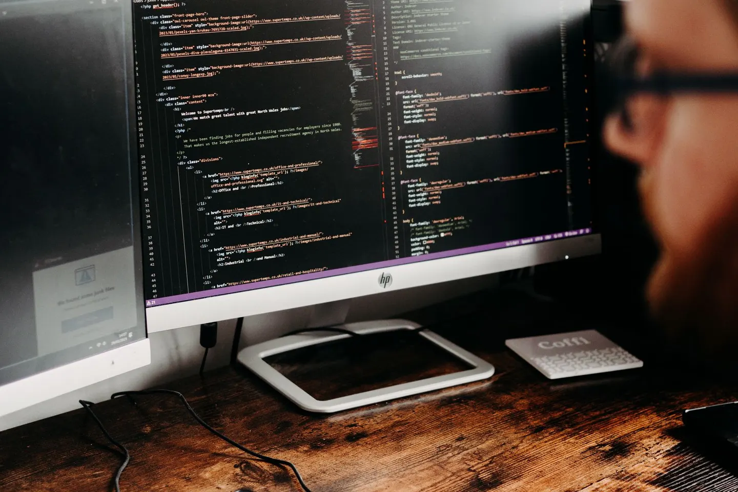 A person faces a desktop monitor displaying lines of code above a wooden desk.