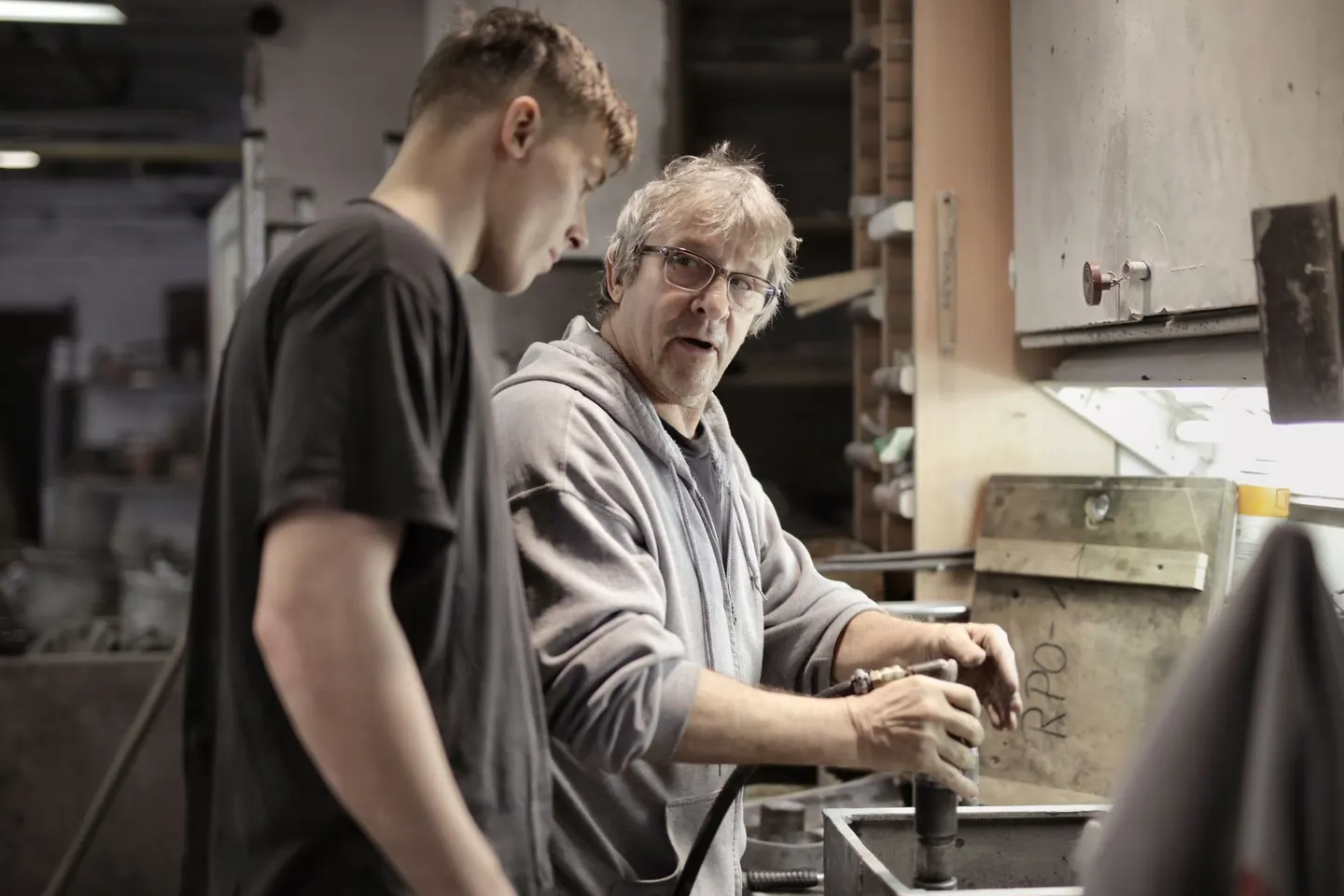 Two people examining a metal component together at a workshop bench.