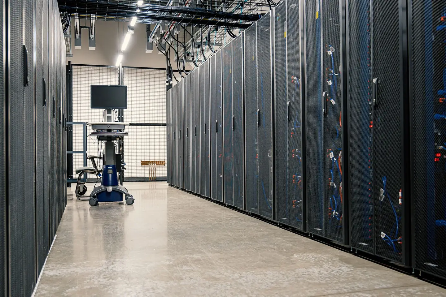 Rows of tall equipment cabinets line a data center aisle with a computer cart.