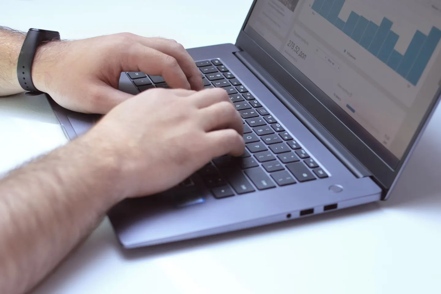 Hands type on a laptop with blue charts displayed on its screen.