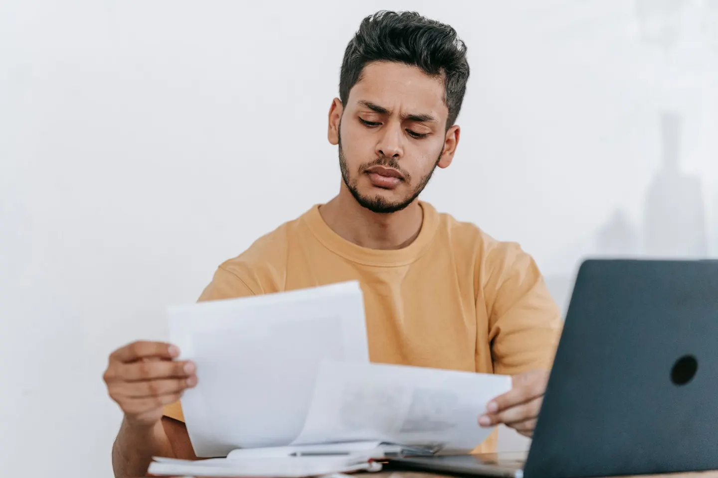A man comparing printed documents beside a laptop at his desk.