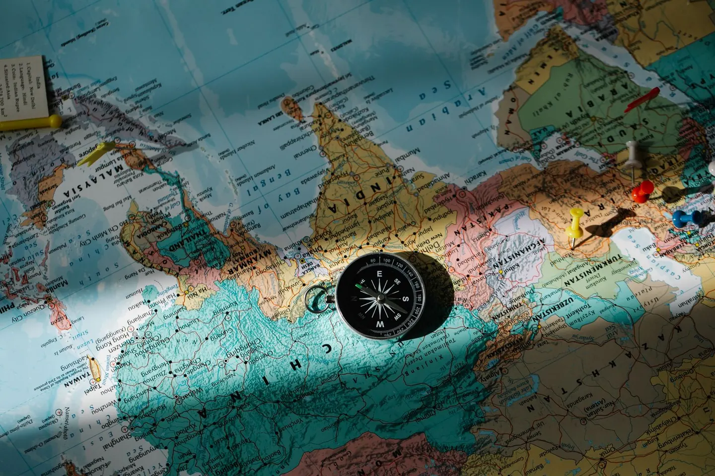 A compass and colored map pins rest on a printed map.