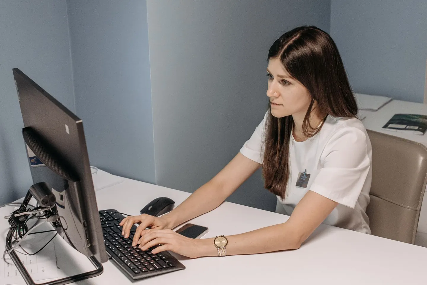 A woman types at a desktop computer on a white desk.