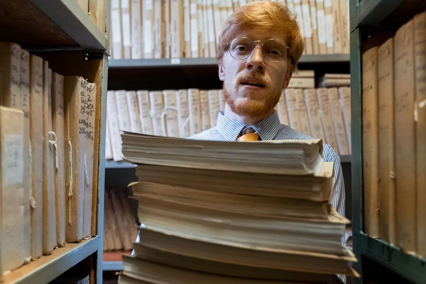 A man carries bound records between shelves of archival documents.
