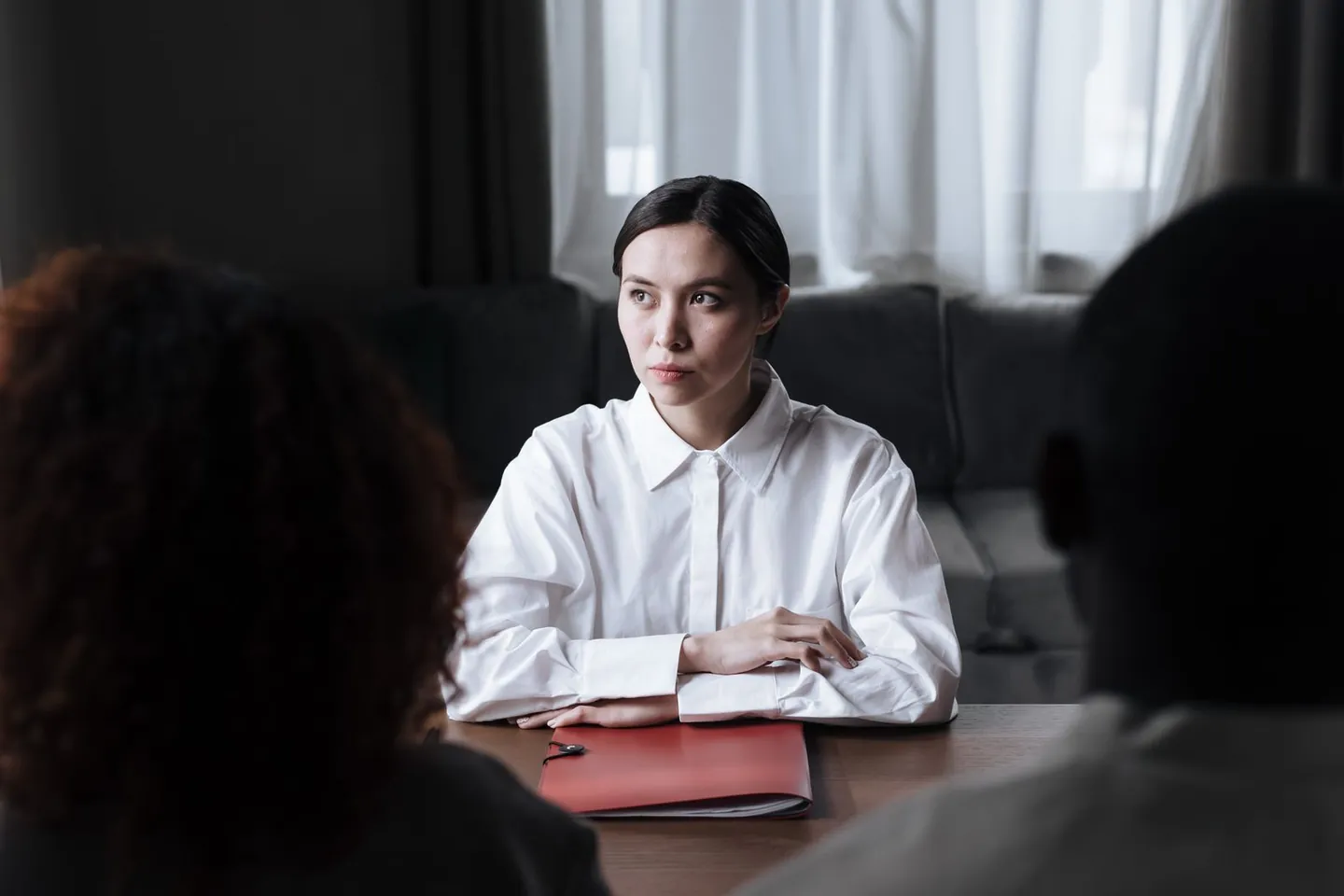 A woman sits across from two people with a document folder on the table.