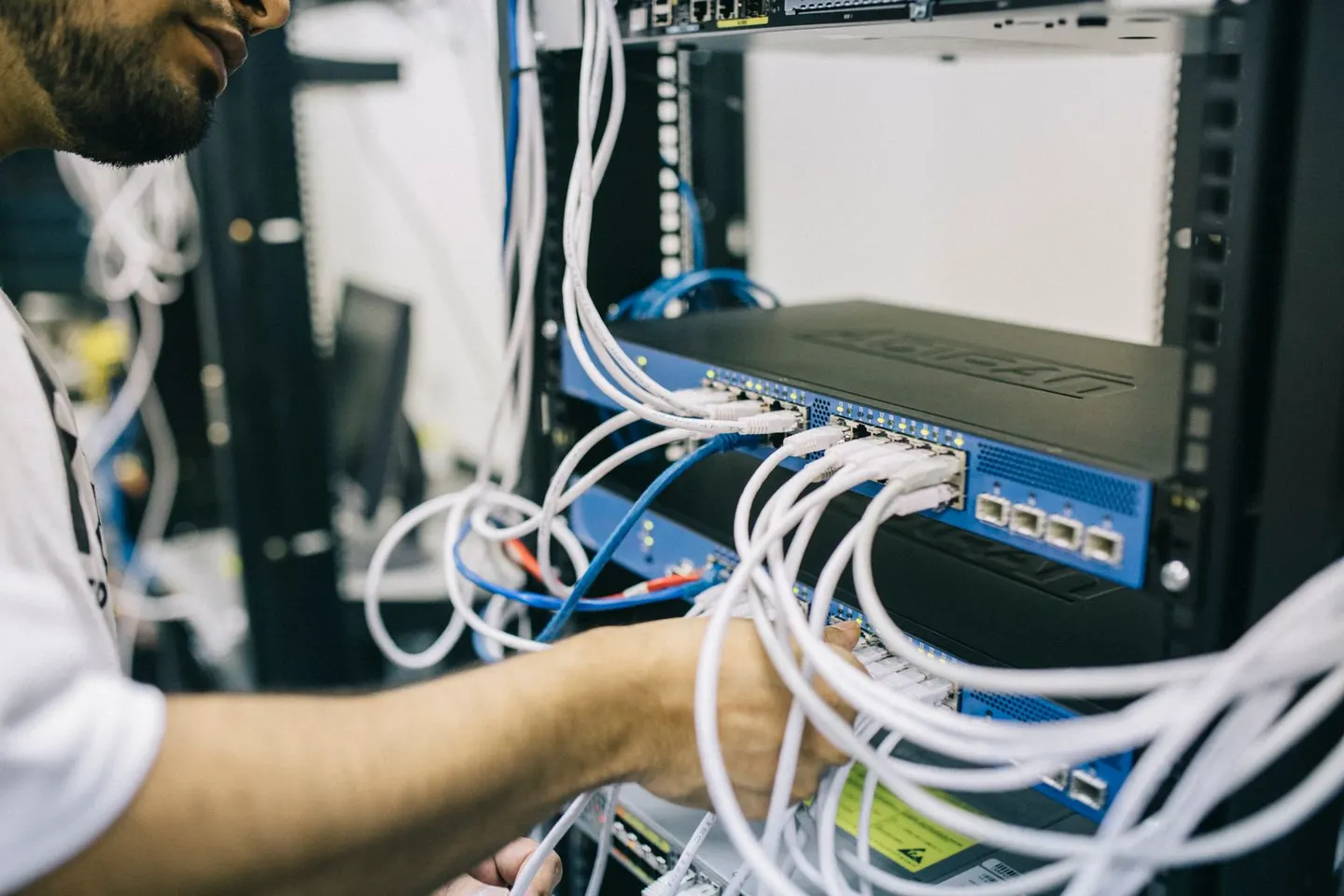 A person adjusts network connections among blue and white cables in an equipment rack.