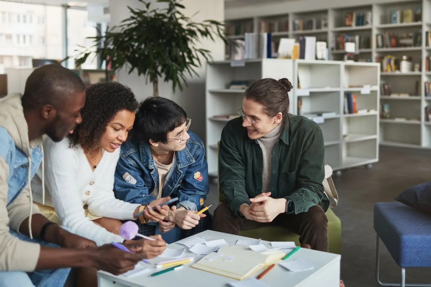 Four adults discuss notes and papers around a table in a library.
