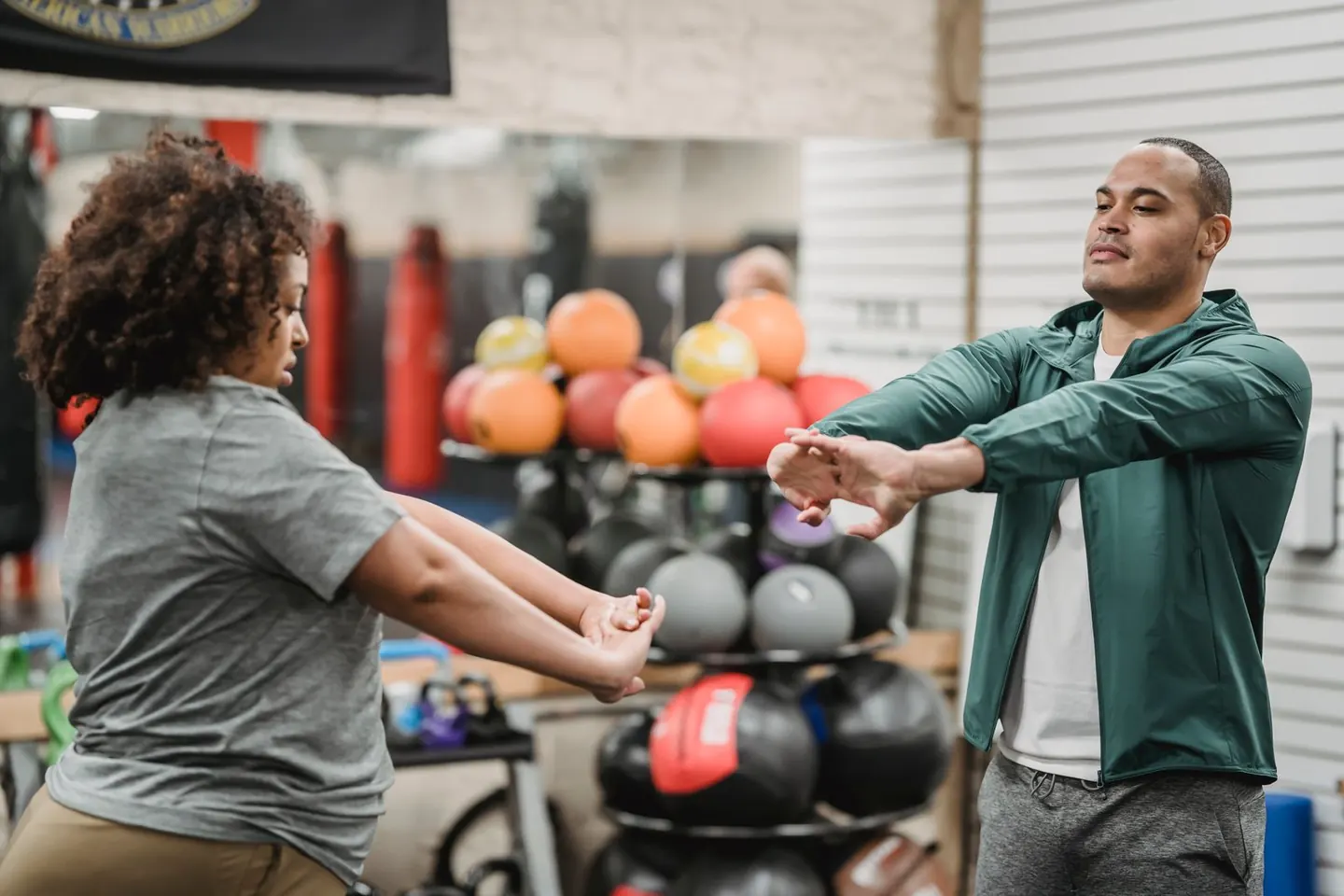 Two adults stretch their arms in a gym with exercise equipment behind them.