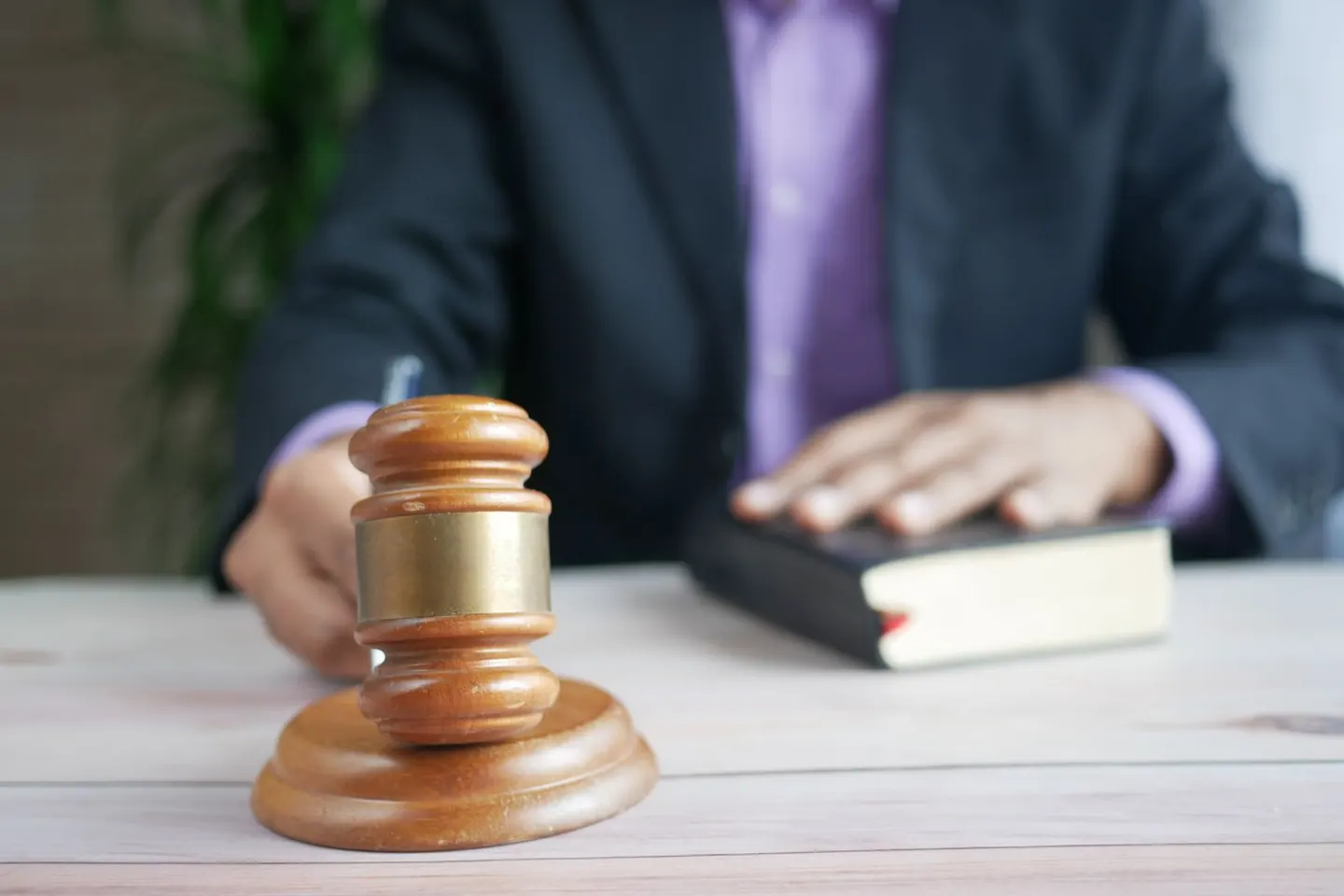 A wooden gavel rests on a table in front of a person and a thick book.
