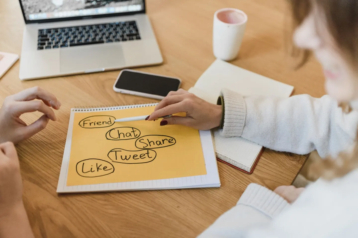 Two people review handwritten social-media ideas beside a laptop and smartphone.