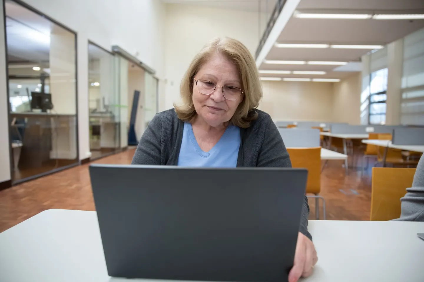 A woman with glasses working on a laptop at a library table.