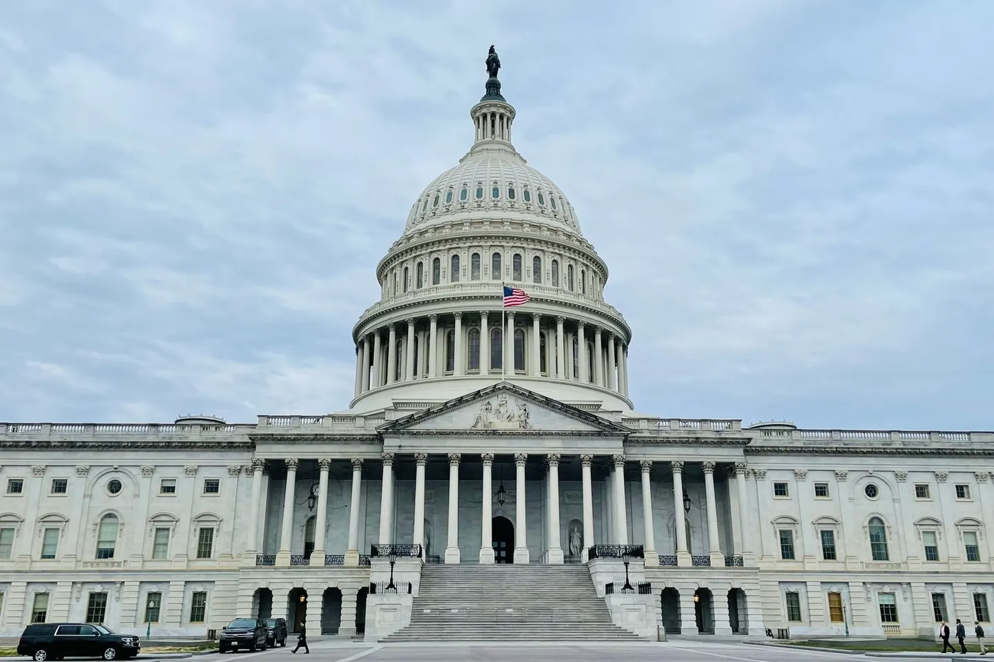 The United States Capitol dome rises above its columned entrance beneath a cloudy sky.