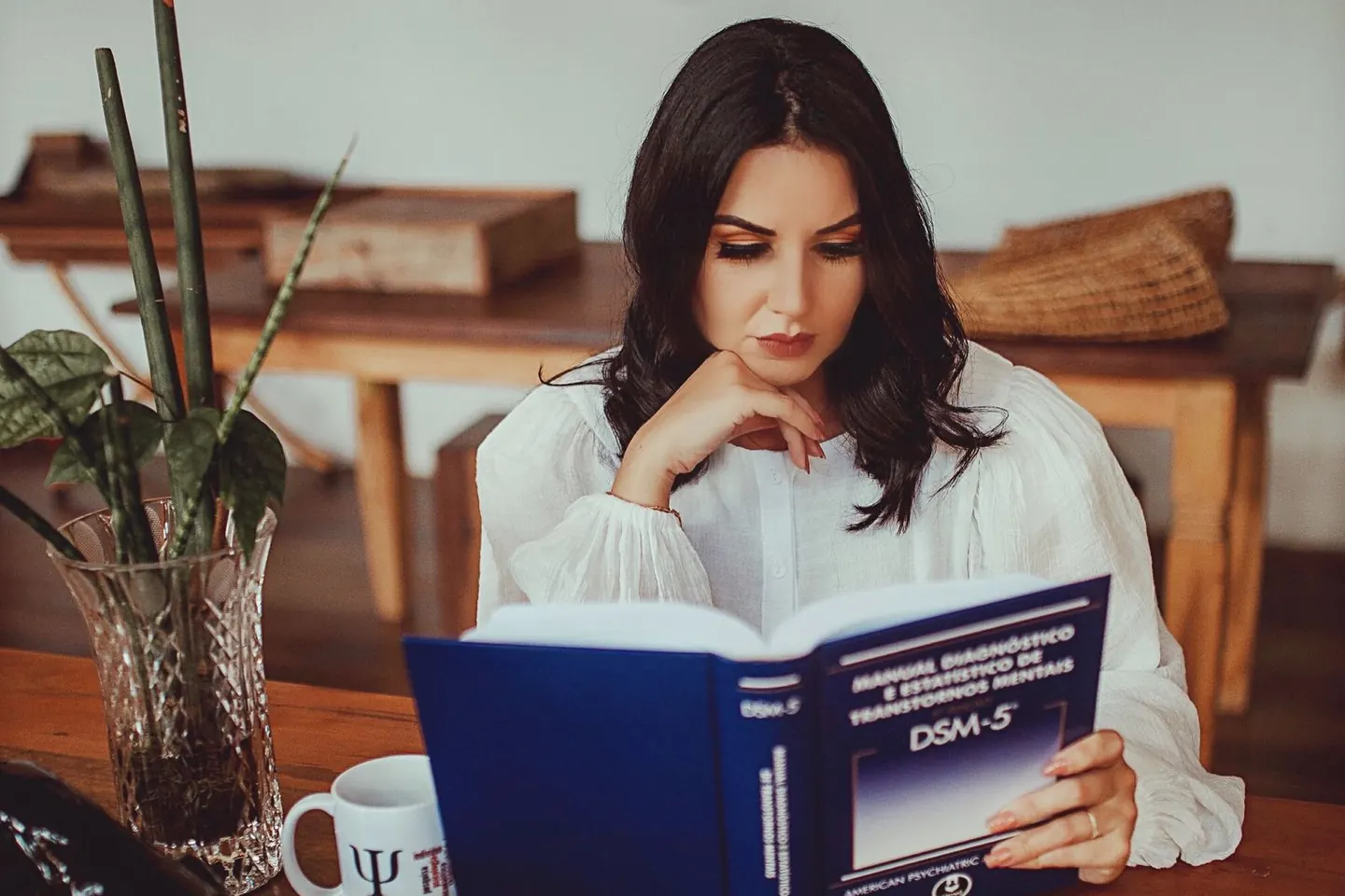 A woman reads a DSM-5 reference book at a wooden desk.
