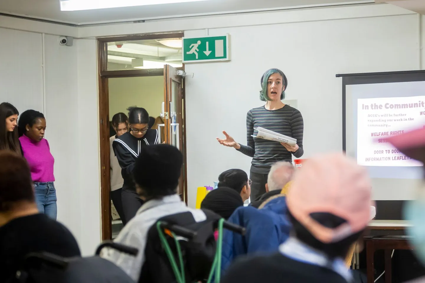 A woman presents community information to a seated group.