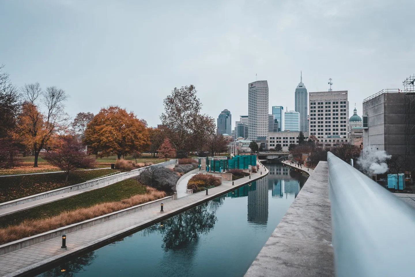 The Indianapolis downtown skyline rises beside the Central Canal walkway and autumn trees in Indiana.