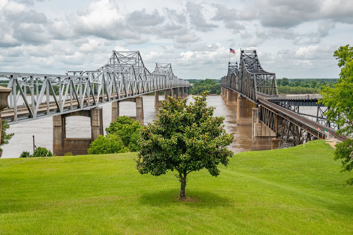 The Vicksburg Bridges cross the Mississippi River beyond a green lawn in Vicksburg, Mississippi.