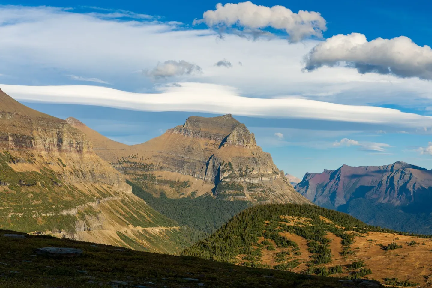 Rugged peaks and green slopes in Glacier National Park under a bright sky in Montana.