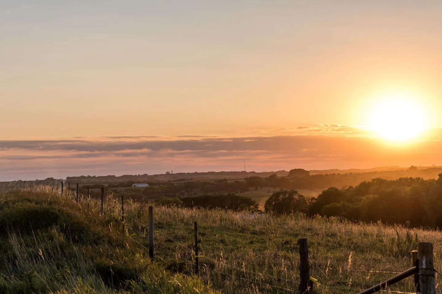 The sun rises over rolling fields and a fence line in rural Nebraska.