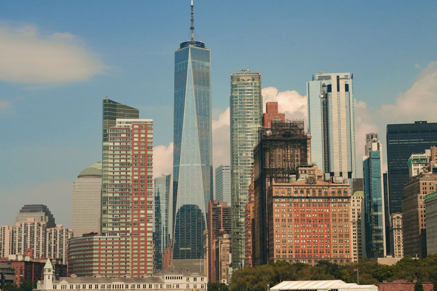 One World Trade Center and lower Manhattan towers rise against a blue sky in New York City.