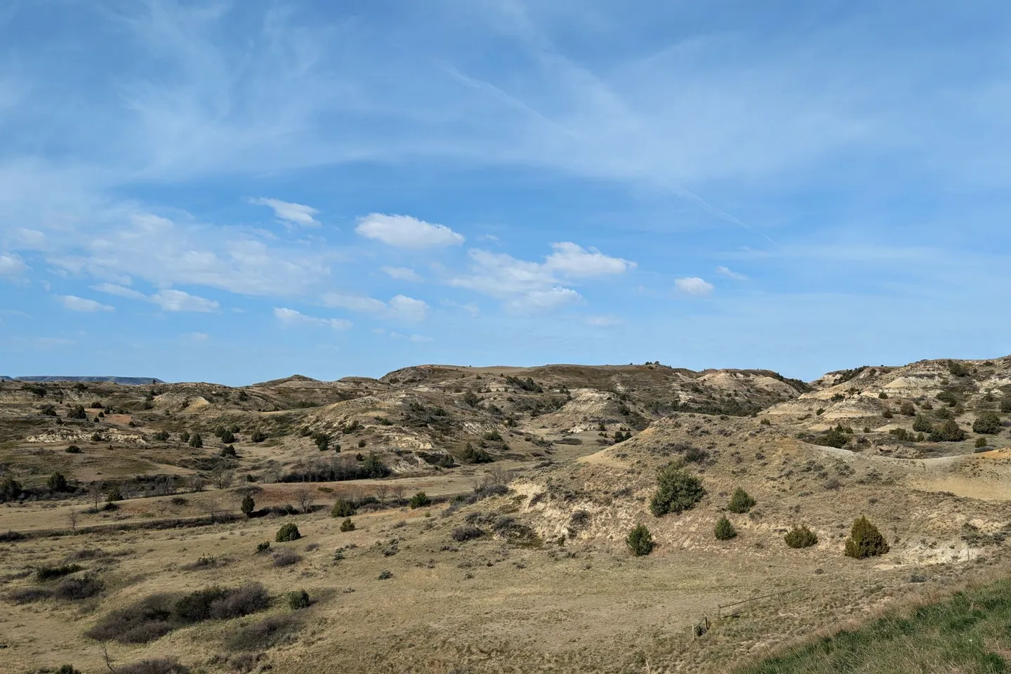 Grassy hills and eroded badlands under a blue sky in western North Dakota.