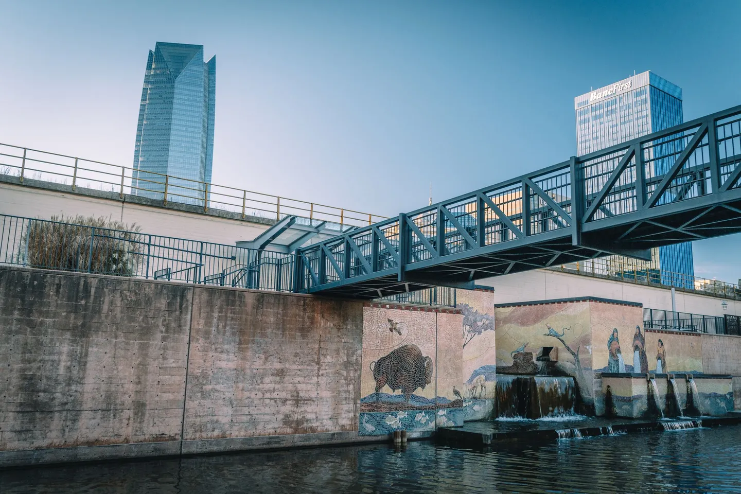 A footbridge and bison murals line the Bricktown canal below downtown towers in Oklahoma City, Oklahoma.