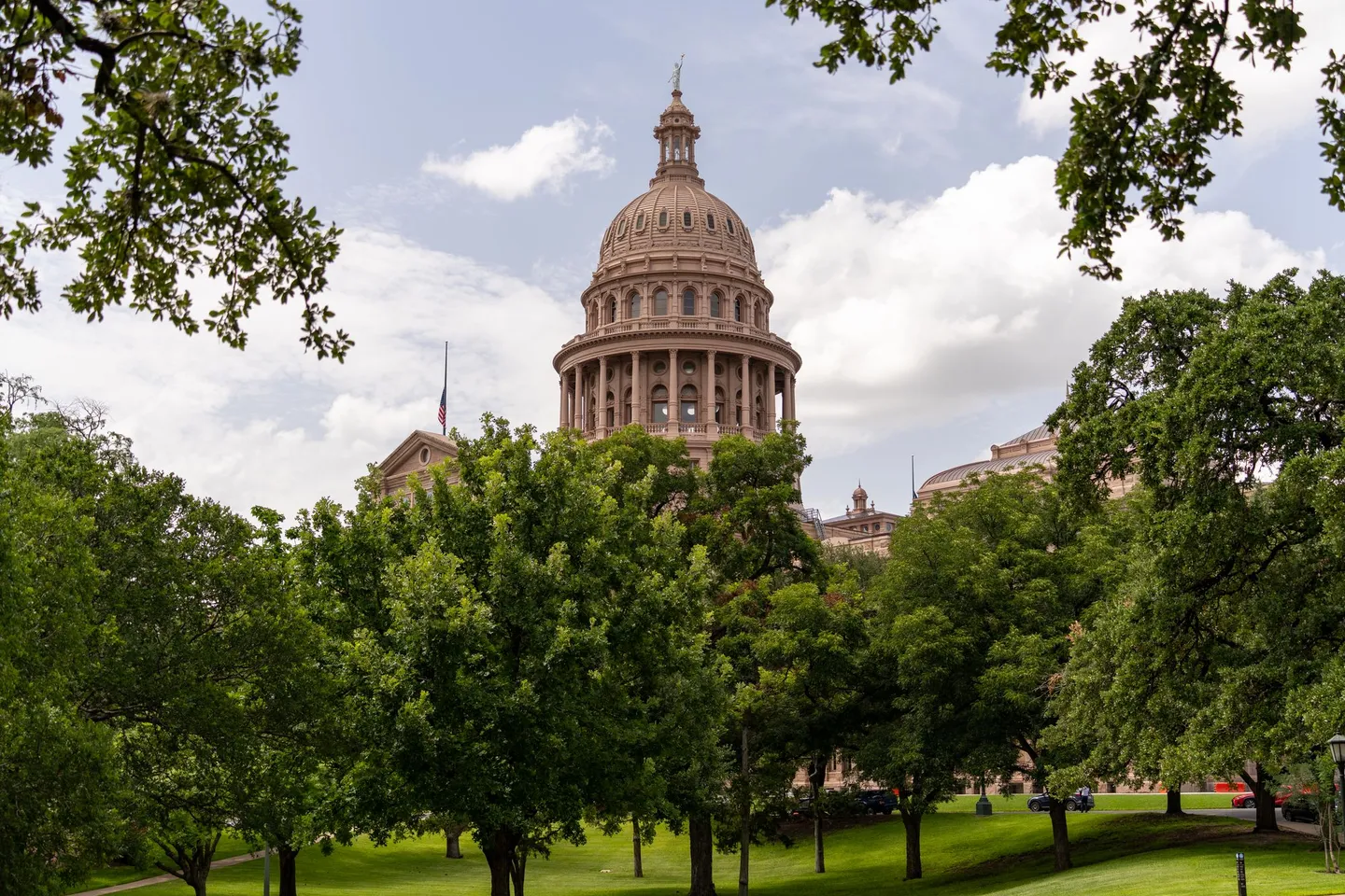 The Texas State Capitol dome rises above green trees and lawn in Austin, Texas.