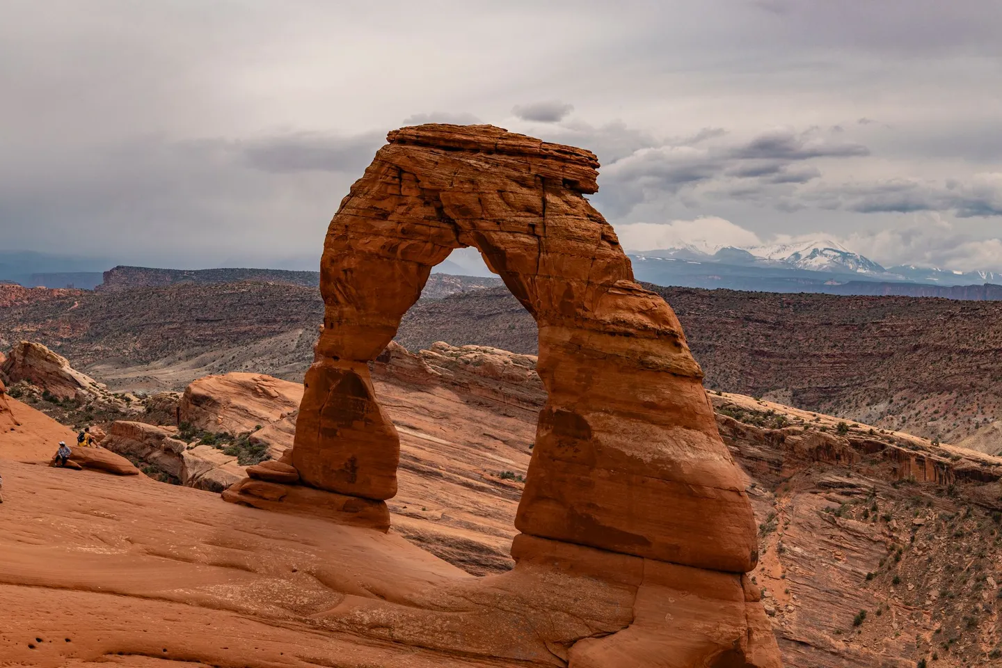 Delicate Arch stands on red slickrock with distant mountains in Arches National Park, Utah.