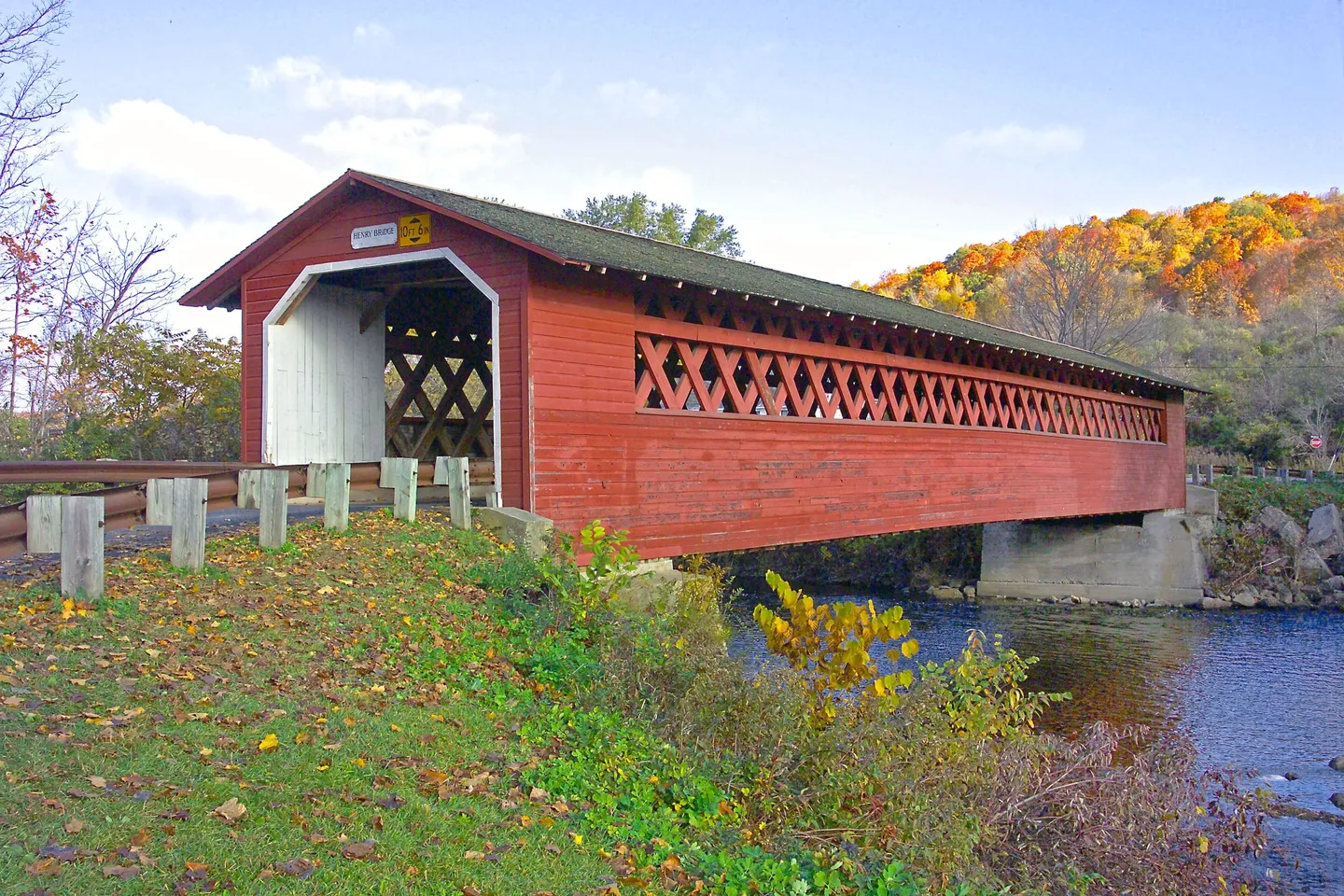 A red covered bridge crosses a river beside autumn foliage in Vermont.